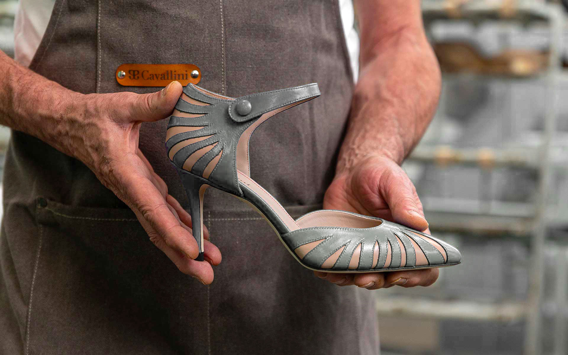 Maestro artigiano Cavallini mentre tiene in mano una scarpa Donna in pelle grigia con tomaio traforato nel laboratorio di Santa Maria a Monte