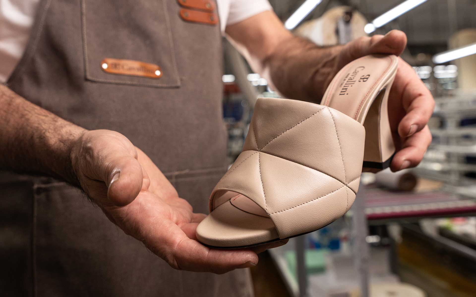 Maestro artigiano Cavallini mentre tiene in mano una scarpa Donna in pelle beige, evidenziando il tomaio con cuciture artigianali nel laboratorio di Santa Maria a Monte