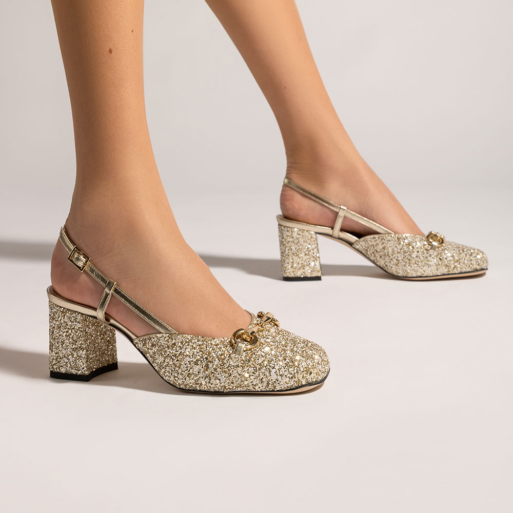 cavallini-ambientata-Franklin Donna che indossa decollete in pelle glitterata oro con tacco quadrato, posizionata su sfondo neutro